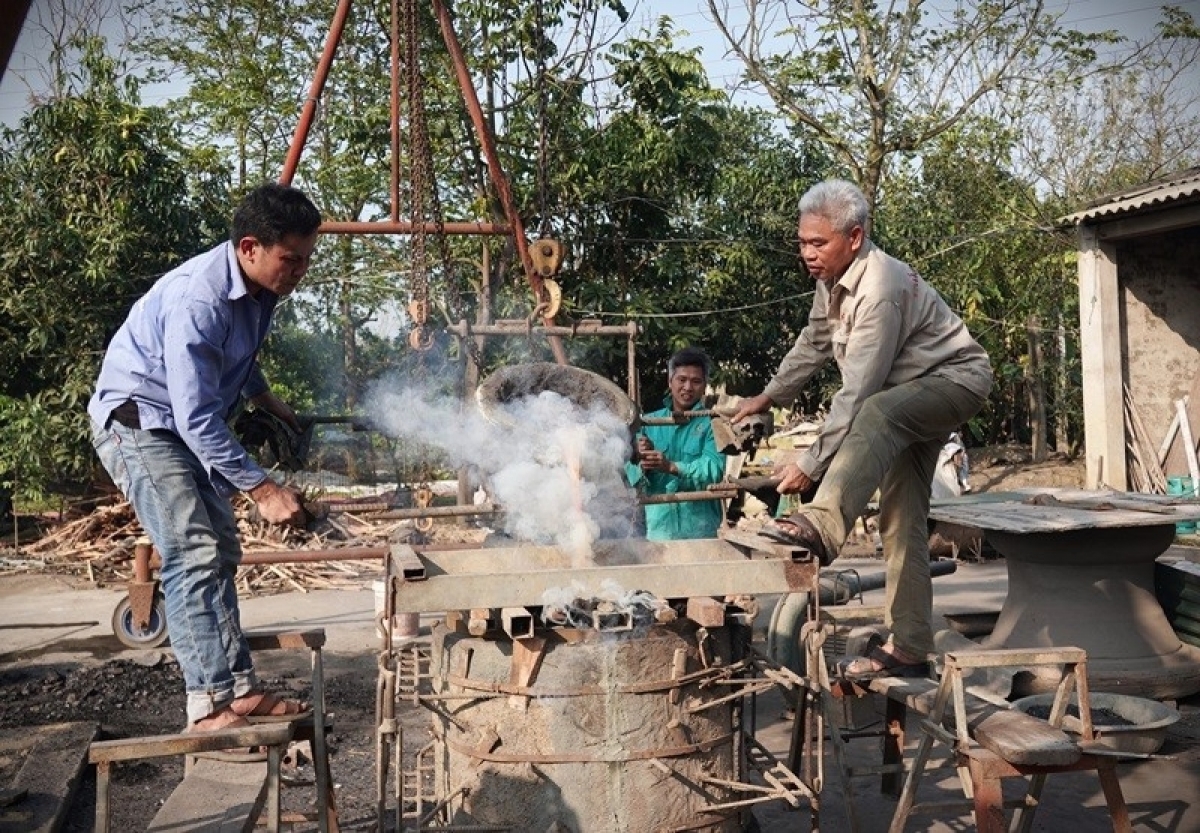 Nghệ nhân Ưu tú Nguyễn Bá Châu (phải) đang thực hiện công đoạn rót đồng nung chảy vào khuôn